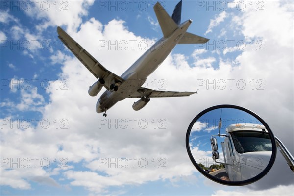 Reflection of semi-truck in side view mirror with plane flying above