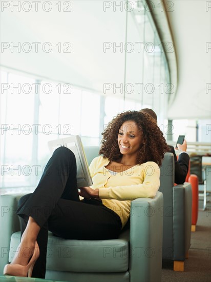 Smiling woman using digital tablet while waiting in lobby