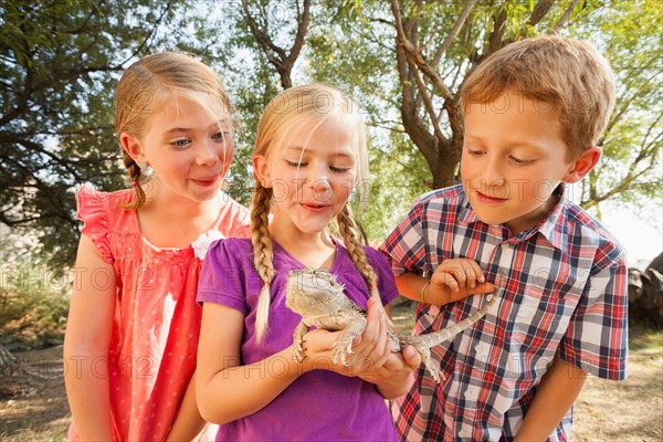 Three kids (4-5, 6-7) excited to be looking at lizard being held by child in the middle