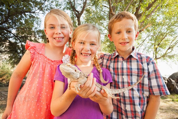 Three kids (4-5, 6-7) excited to be looking at lizard being held by child in the middle