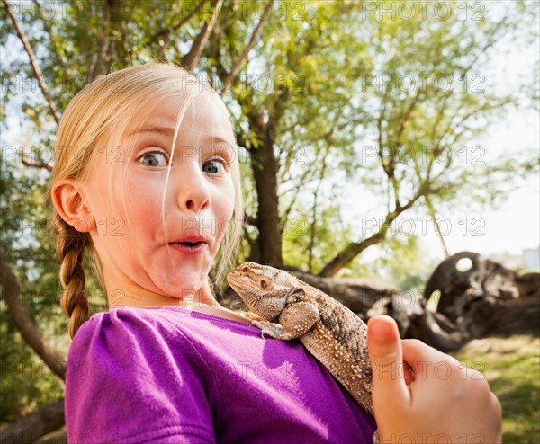 Little girl (4-5) surprised by lizard she is holding