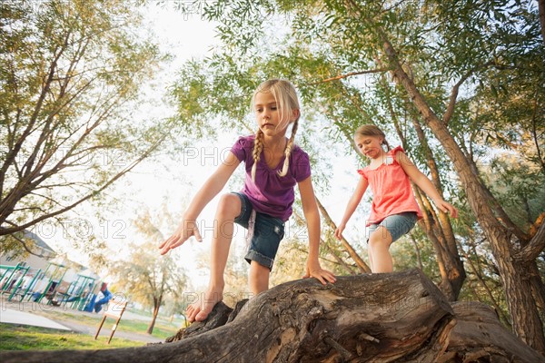 Two little girls (4-5, 6-7) climbing on very large tree branch