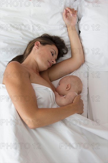 Mother breastfeeding baby daughter (6-11 months) in bed