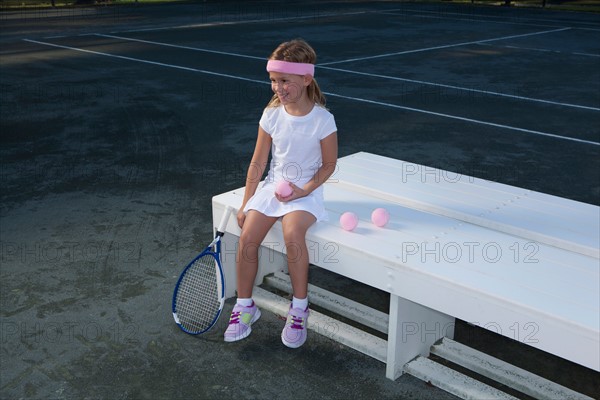 Girl sitting on bench and holding tennis racket