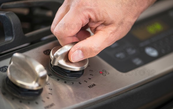 Close-up of hand adjusting stove burner.