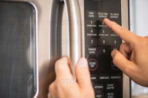 Close-up of hand using microwave oven.