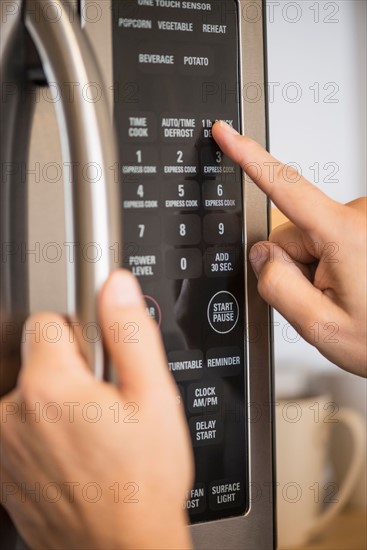 Close-up of hand using microwave oven.