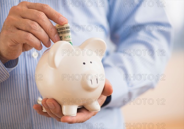 Man inserting money into piggy bank.