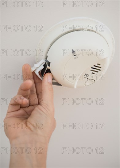 Hand changing battery in smoke alarm.