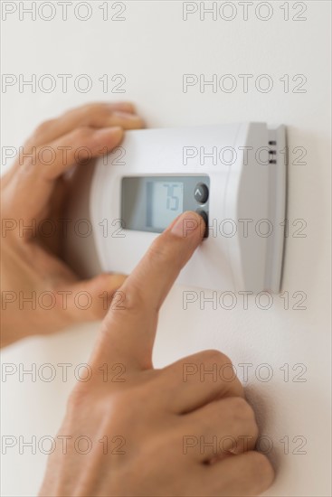 Hand changing settings on air conditioning thermostat.