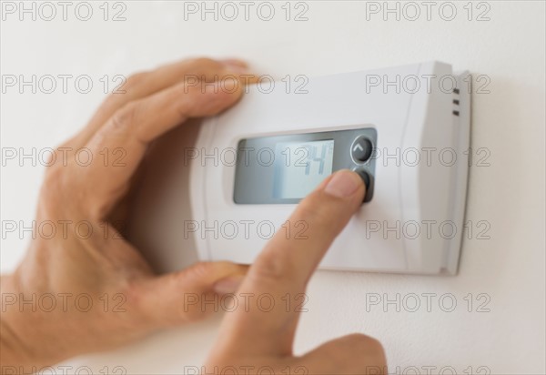 Hand changing settings on air conditioning thermostat.