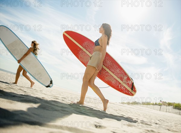 Two women carrying surfboards on beach. Photo: Jamie Grill