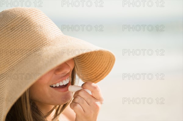 Woman wearing sun hat applying lipstick. Photo : Jamie Grill
