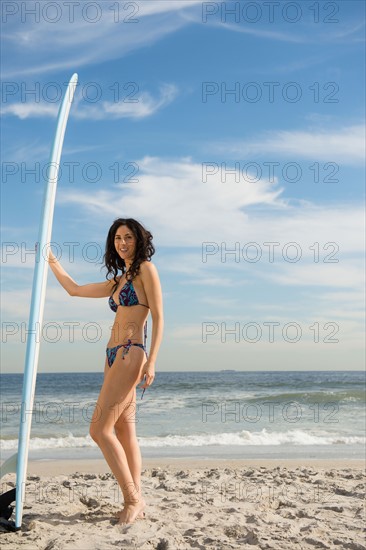 Woman holding surfboard at beach. Photo : Jamie Grill