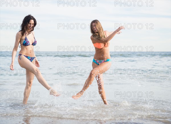 Two young women splashing water on beach. Photo : Jamie Grill