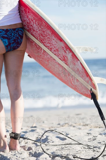 Woman carrying surfboard on beach. Photo: Jamie Grill