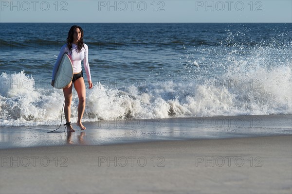 Woman carrying surfboard on beach. Photo : Jamie Grill
