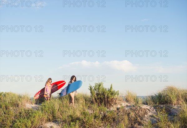 Two female surfers walking on beach. Photo : Jamie Grill