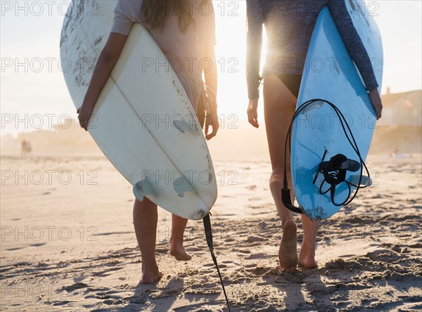 Two female surfers walking on beach. Photo : Jamie Grill