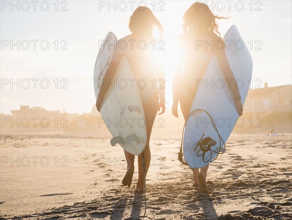 Two female surfers walking on beach at sunset. Photo: Jamie Grill