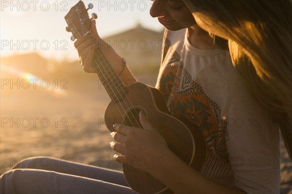Woman playing ukulele at sunset. Photo : Jamie Grill