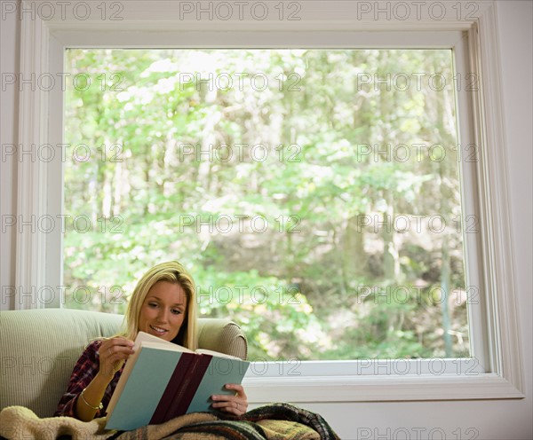 Woman sitting on sofa and reading book. Photo : Jamie Grill