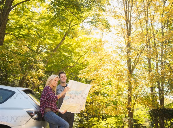 Couple leaning against car and reading map. Photo : Jamie Grill