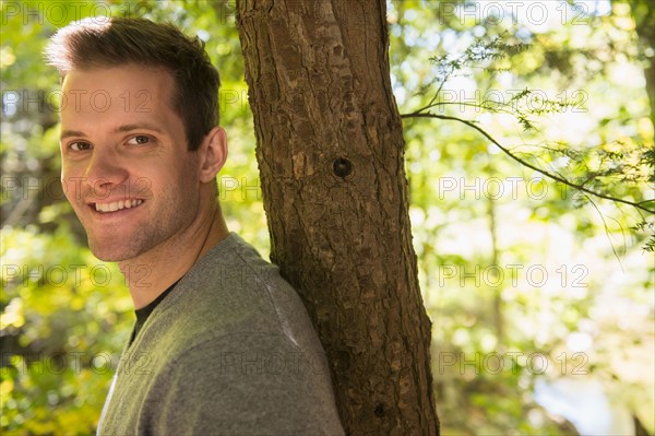 Portrait of young man leaning against tree trunk. Photo : Jamie Grill