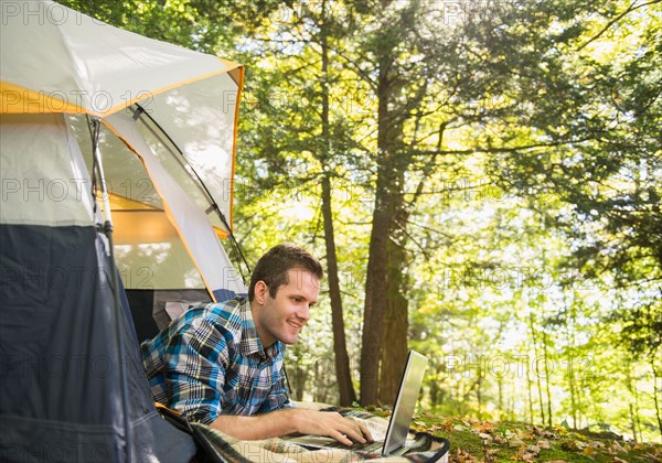 Man using laptop outside tent. Photo : Jamie Grill