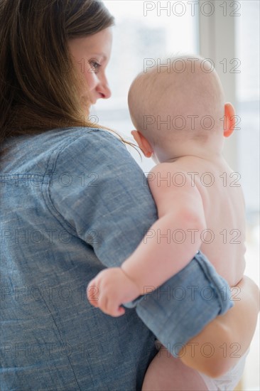 Mother holding baby boy (2-5 months) by window. Photo: Jamie Grill