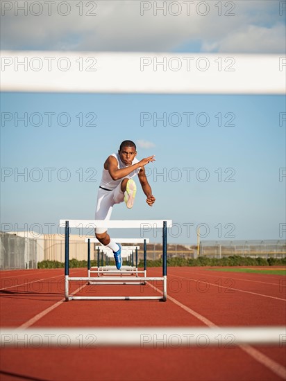 Boy (12-13) hurdling on running track.