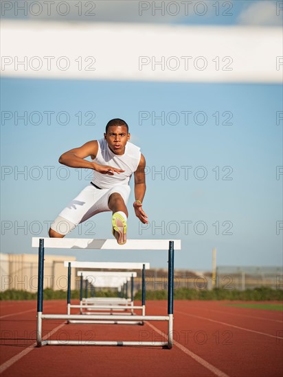 Boy (12-13) hurdling on running track.