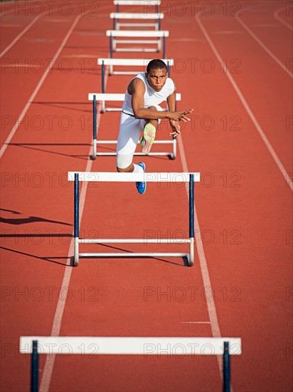 Boy (12-13) hurdling on running track.