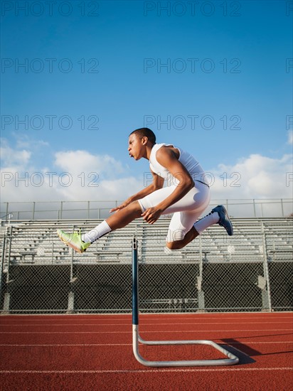 Boy (12-13) hurdling on running track.