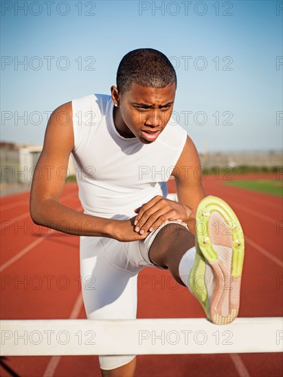 Boy (12-13) stretching on hurdle on running track.