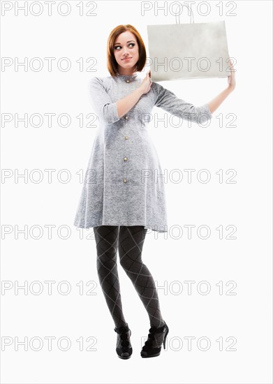 Young woman holding shopping bag, studio shot. Photo : Mike Kemp