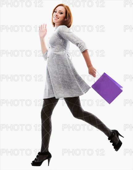 Young woman running with shopping bag, studio shot. Photo: Mike Kemp