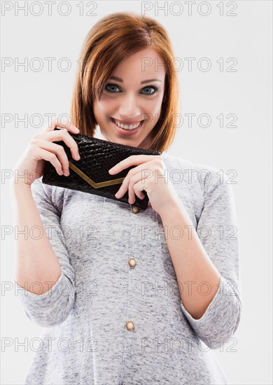 Portrait of young woman showing purse, studio shot. Photo: Mike Kemp
