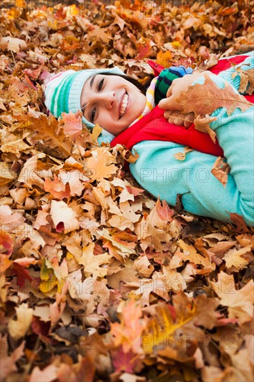 Portrait of smiling young woman lying on autumn leaves . Photo: Mike Kemp