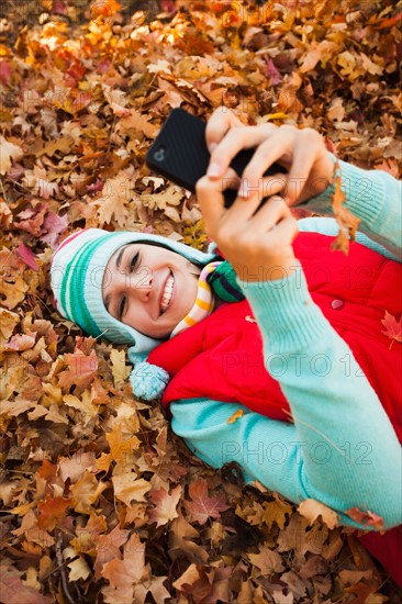 Young woman lying on autumn leaves and using . Photo : Mike Kemp