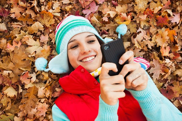 Young woman lying on autumn leaves and using . Photo : Mike Kemp