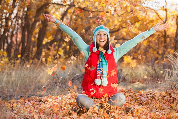 Happy young woman sitting on autumn leaves in forest. Photo : Mike Kemp