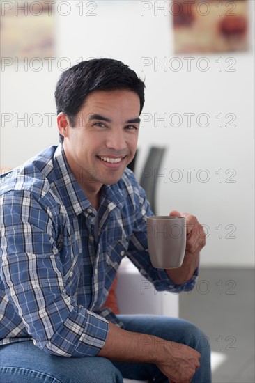 Portrait of man drinking coffee in living room. Photo : Dan Bannister