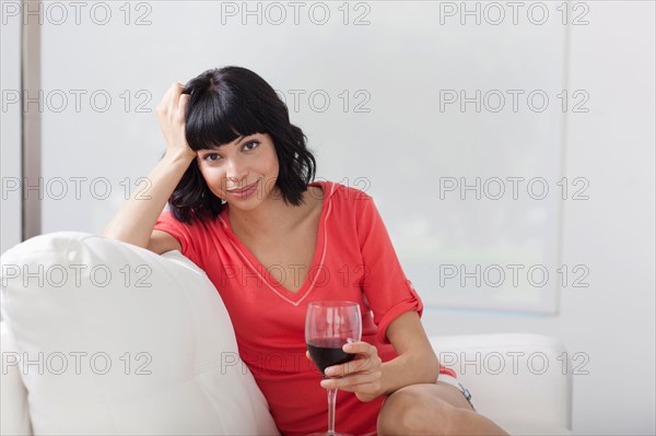 Young woman sitting on sofa with glass of wine. Photo : Dan Bannister