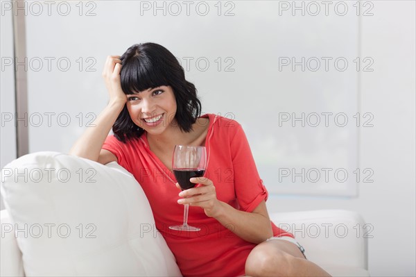 Young woman sitting on sofa with glass of wine. Photo : Dan Bannister