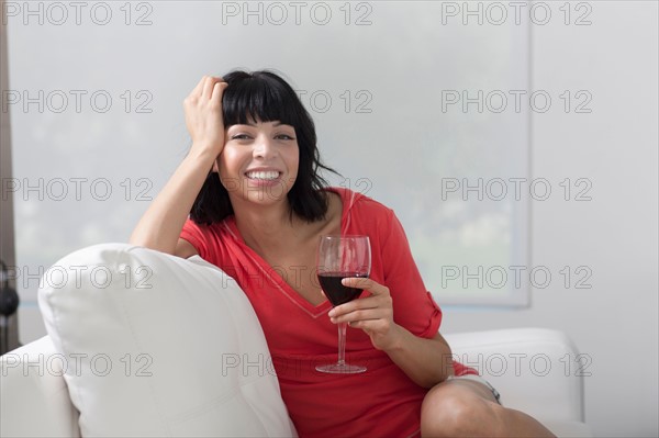 Young woman sitting on sofa with glass of wine. Photo : Dan Bannister