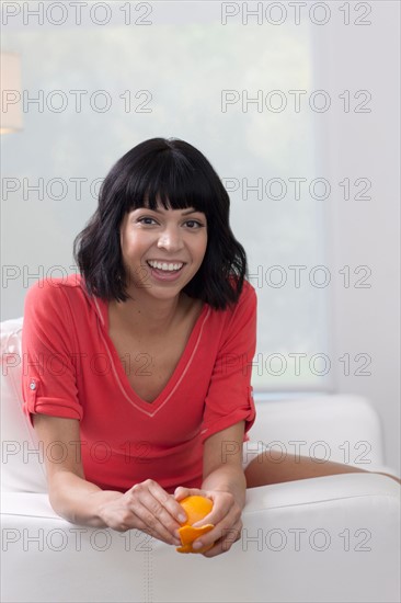Young woman sitting on sofa and eating orange. Photo: Dan Bannister