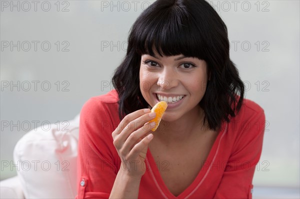 Young woman sitting on sofa and eating orange. Photo: Dan Bannister