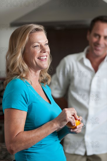 Portrait of mature woman eating orange, man in background. Photo : Dan Bannister