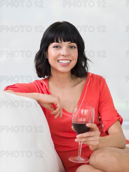 Young woman sitting on sofa with glass of wine. Photo : Dan Bannister